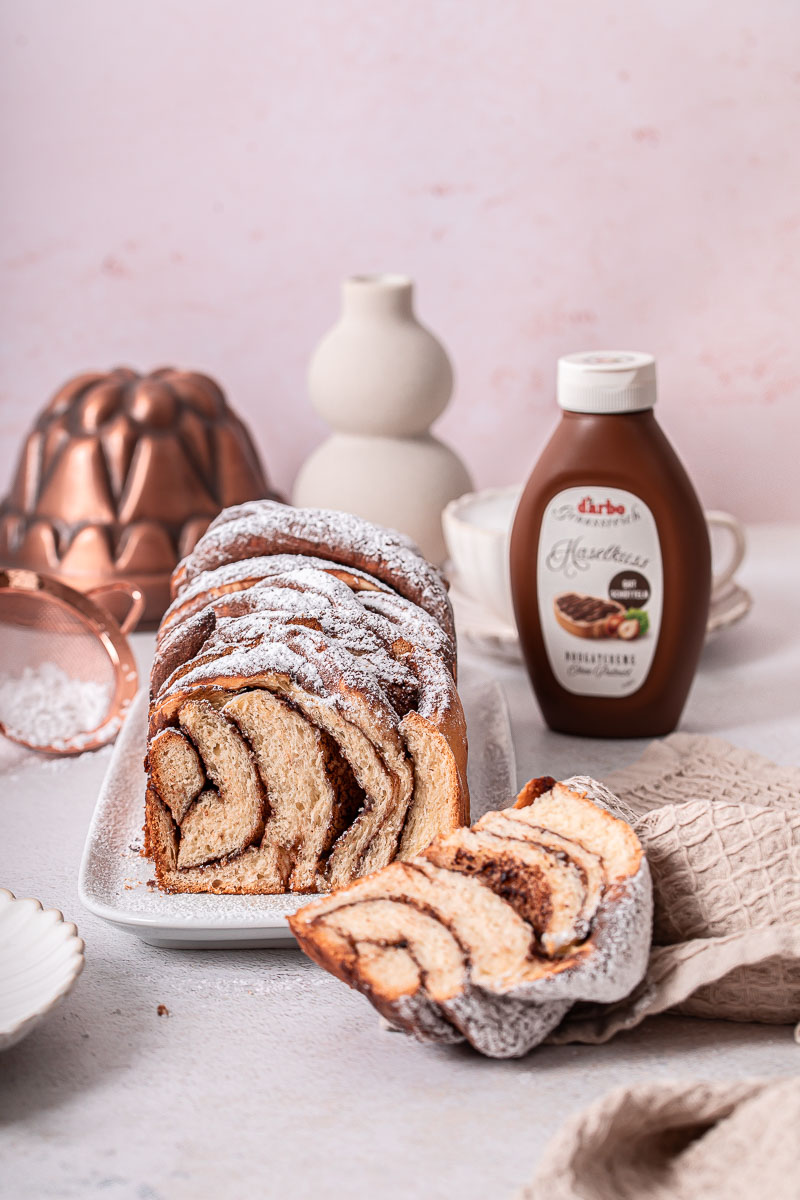 Babka im Anschnitt mit Haselkuss im Hintergrund